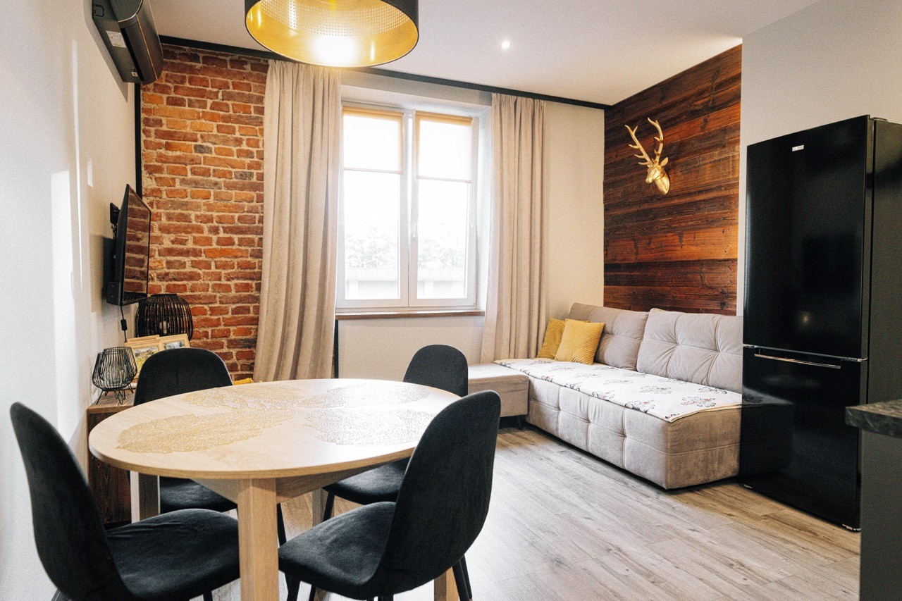 Apartament Halny — salon z ceglaną ścianą, jadalnią i wypoczynkiem przy oknie