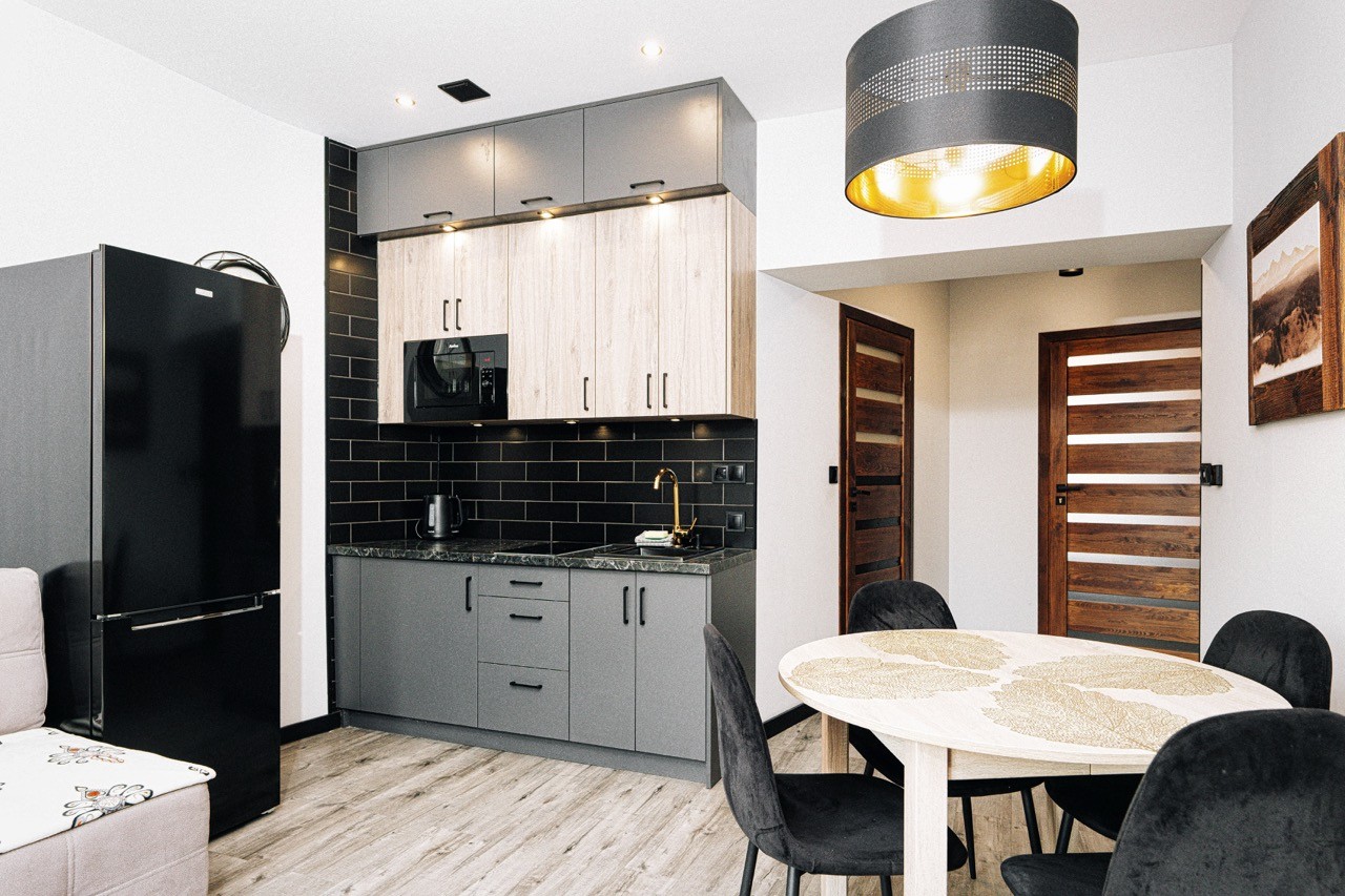 Aneks kuchenny w apartamencie Halny — czarna zabudowa, lodówka i okrągły stół z krzesłami