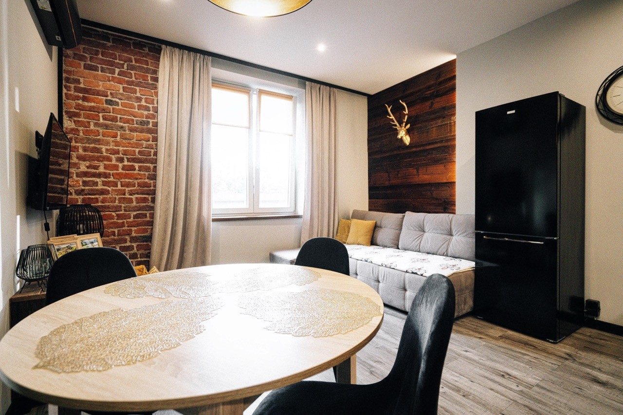 Apartament Halny — okrągły stół jadalniany na tle ceglanej ściany i sofy