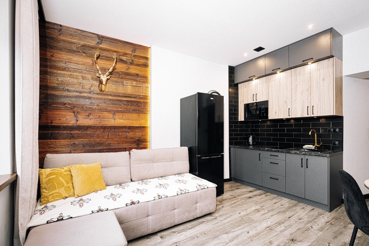 Salon apartamentu Halny — narożna sofa, drewniana ściana z porożem i kuchnia w tle
