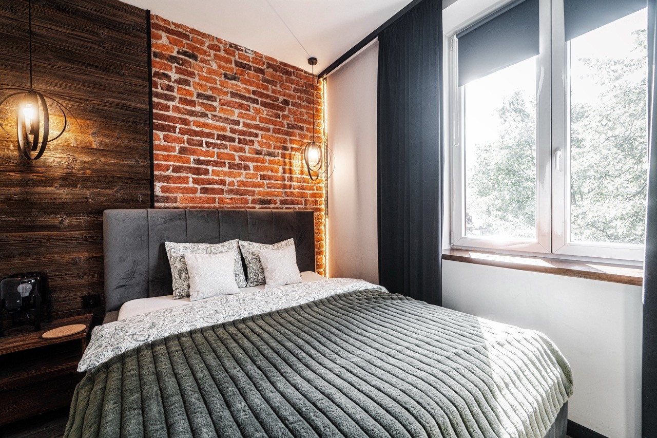 Jasna sypialnia z dużym łóżkiem i ceglaną ścianą w apartamencie Watra