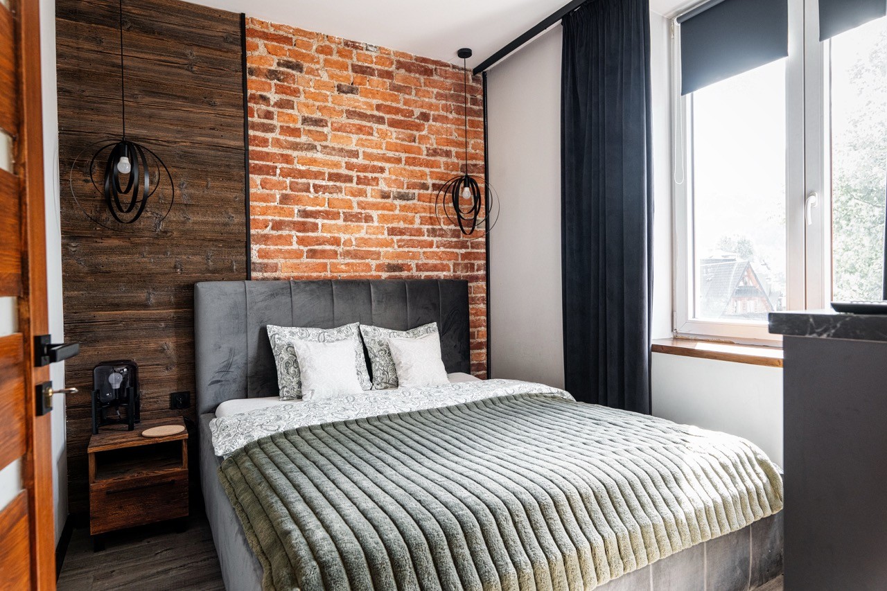 Sypialnia z łóżkiem dwuosobowym i ceglaną ścianą w apartamencie Watra